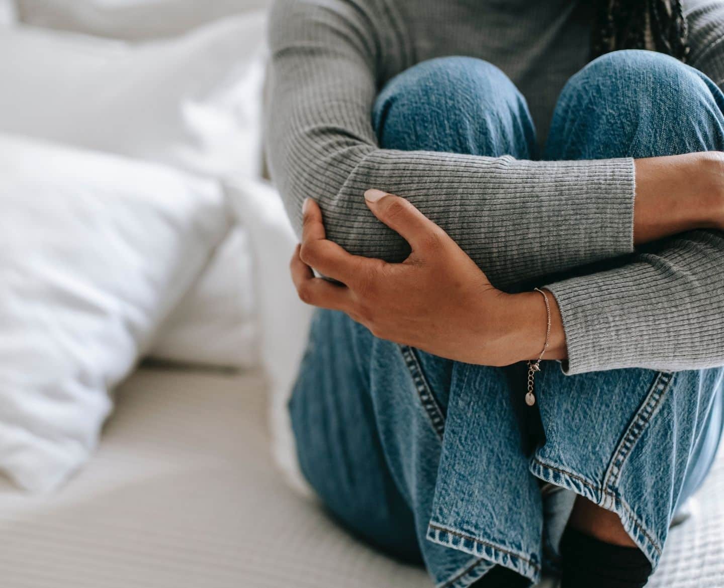 woman sits holding knees on bed Motherly