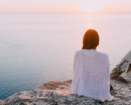 Woman looking out at sunrise over water possibly contemplating the link between miscarriage risk and extreme heat