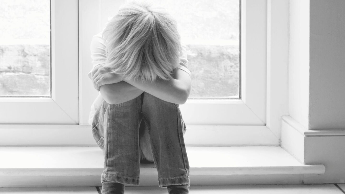 black and white photo of little boy sitting with his head in his arms