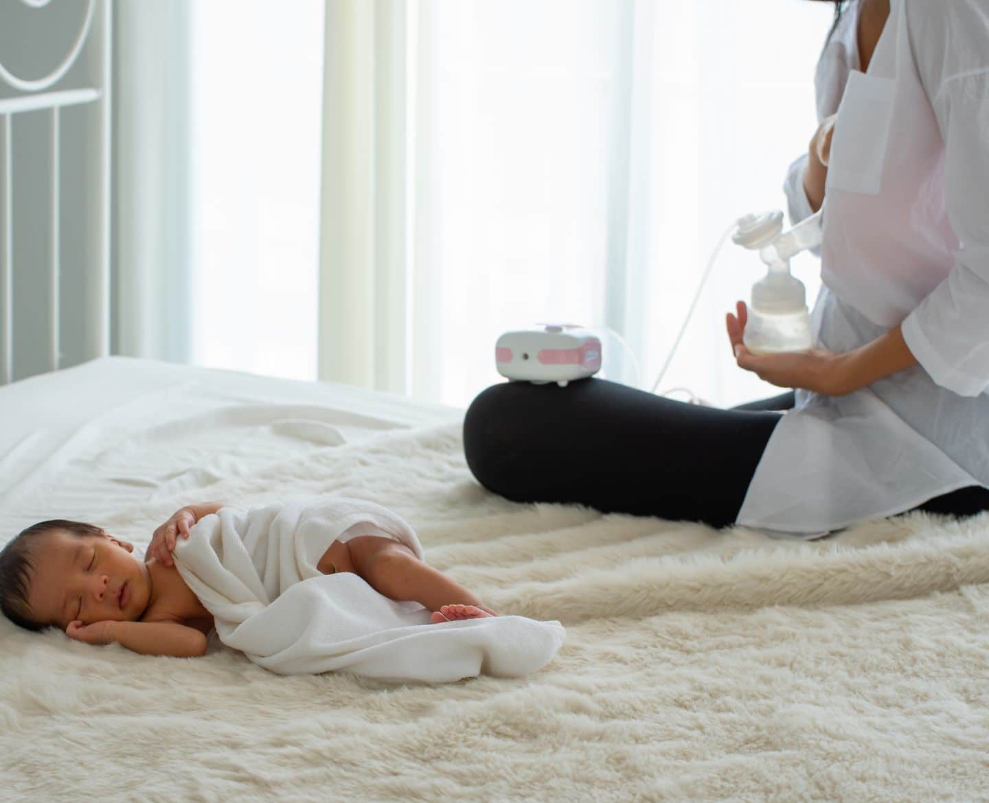 mom exclusively pumping while baby lays on bed