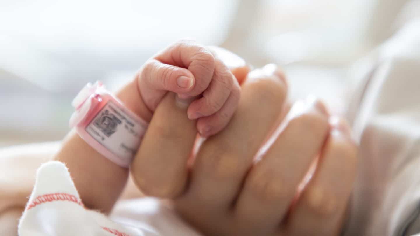 newborn baby wearing a hospital band clutching mom's finger