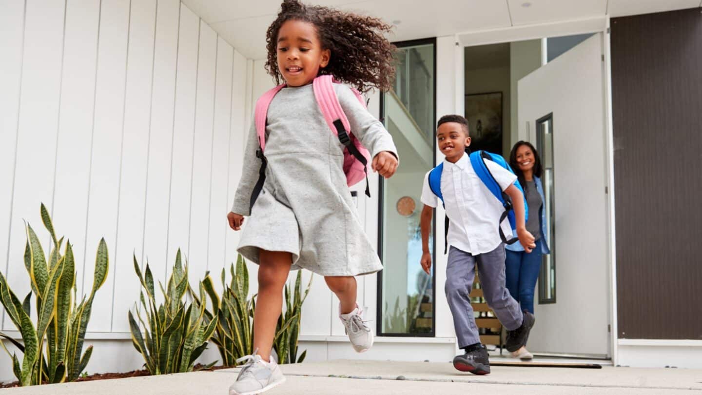 two children going back to school while mom looks on smiling