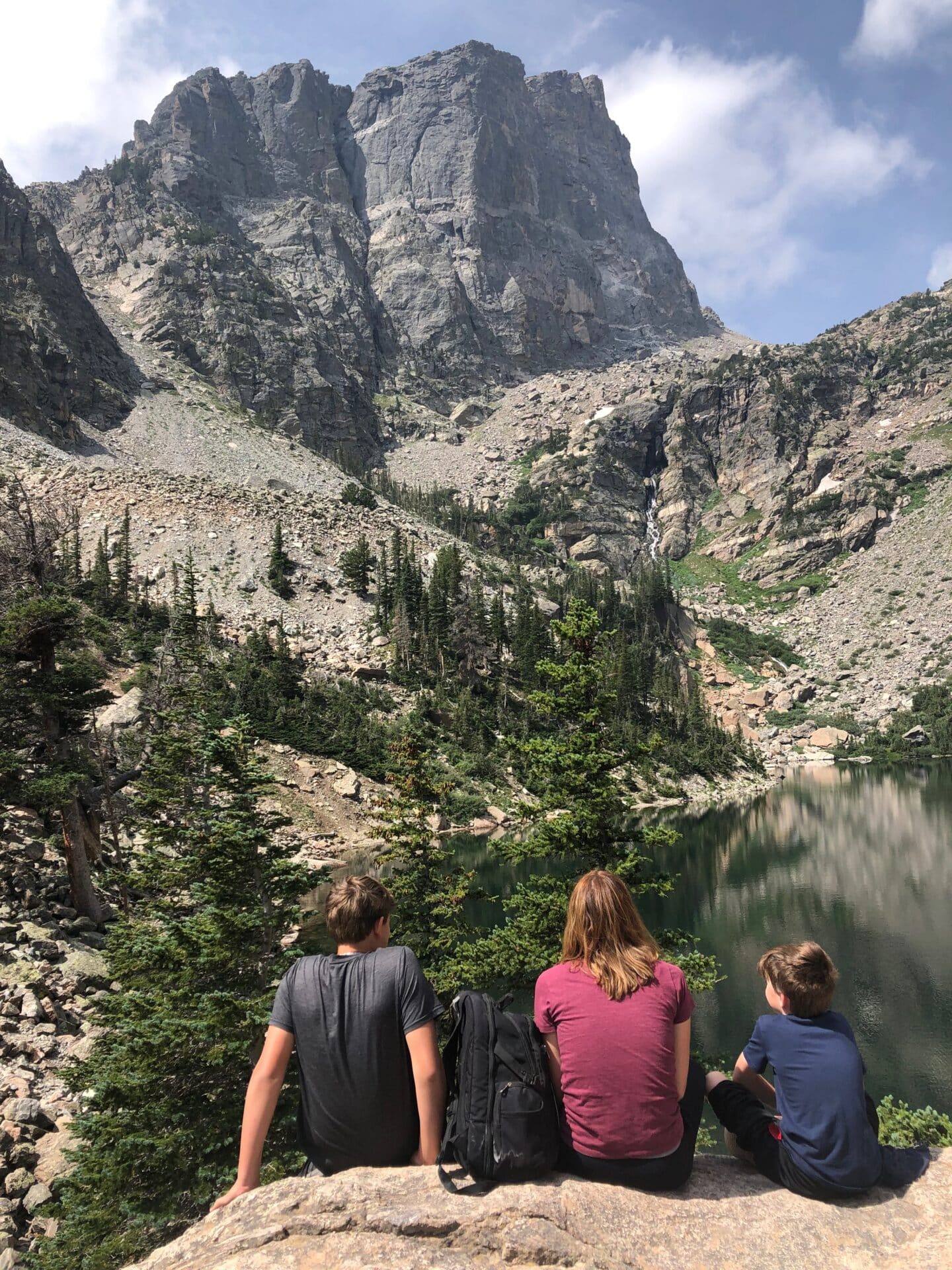 Mom and two boys sitting on a large rock, looking at lake and mountains