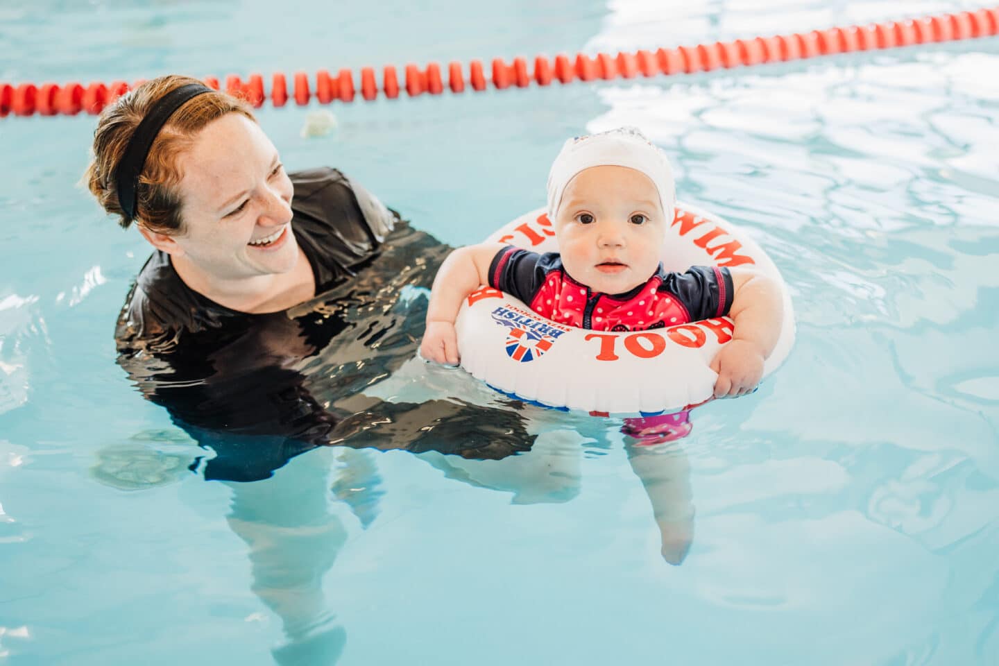 baby swimming in a tube in the pool getting assisted by a swim coach