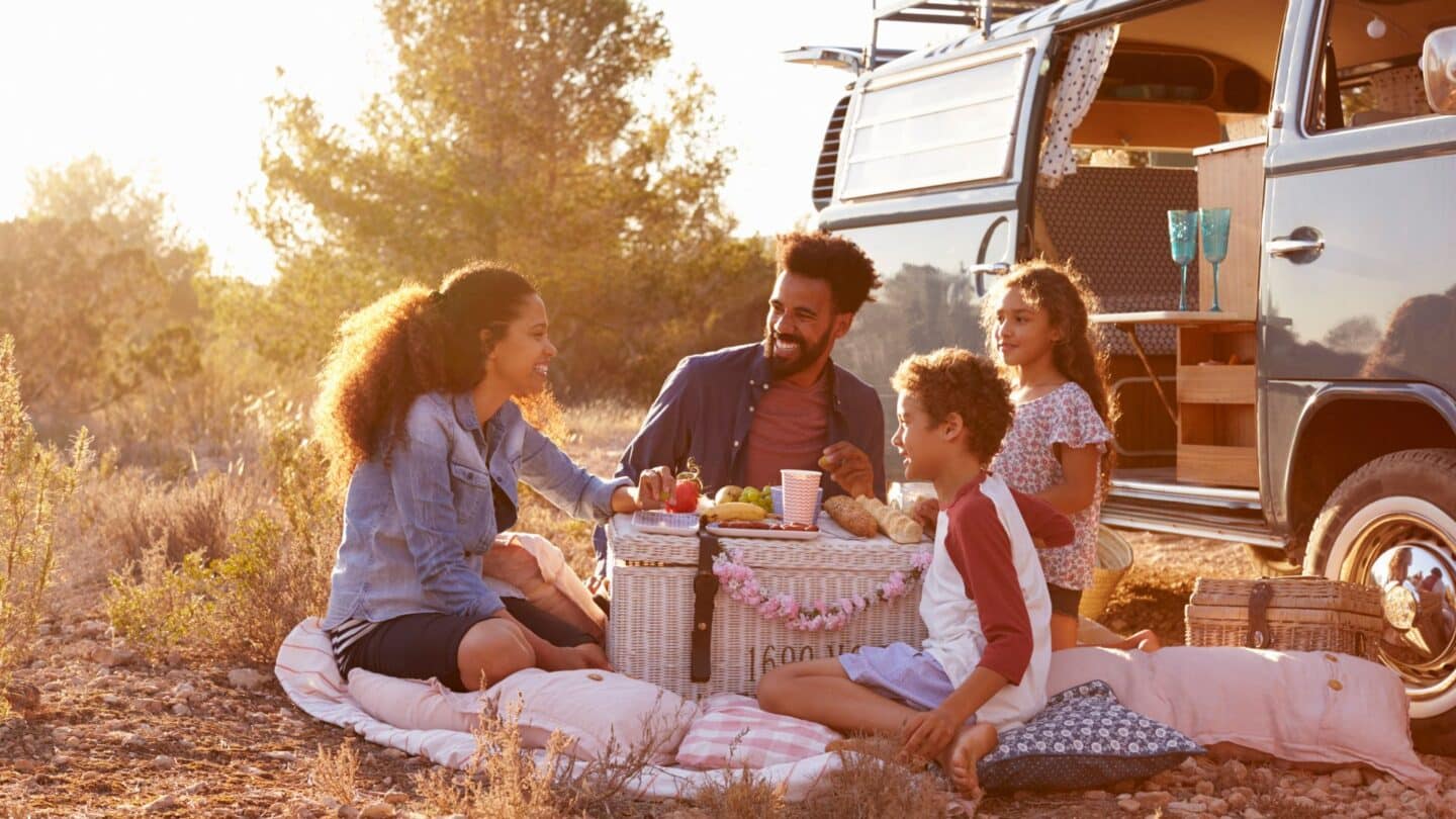 happy family eating outside car while on road trip, because travel with kids boosts happiness