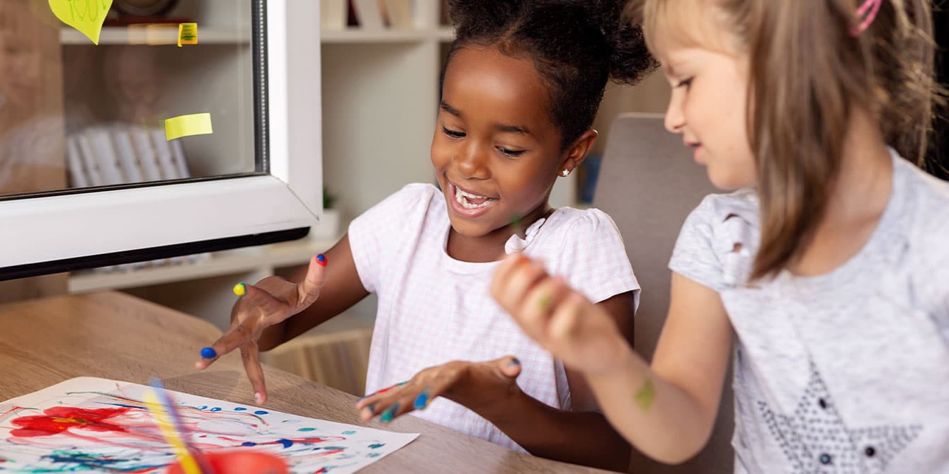 two girls sitting at a table, learning how to make finger paint