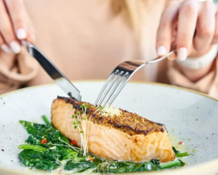 woman cutting baked salmon eating fish during pregnancy 1440x670 1