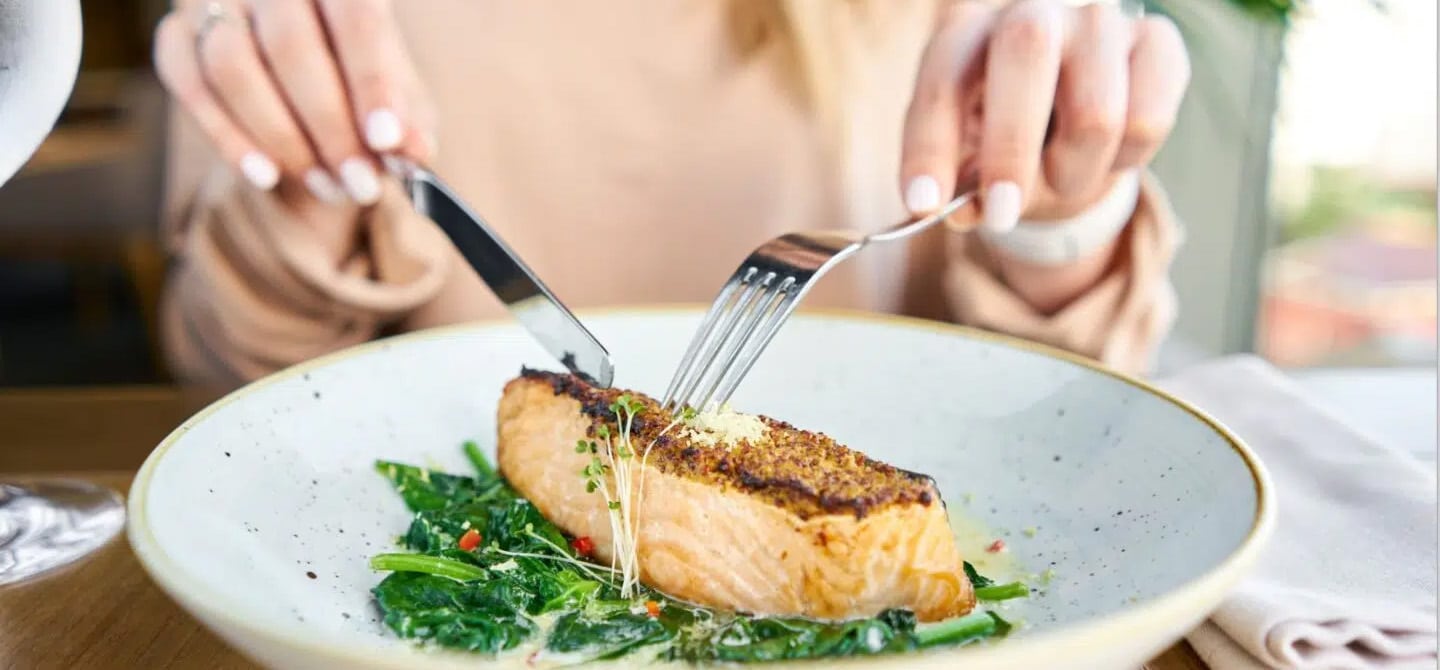 Woman cutting baked Salmon - can you eat fish during pregnancy