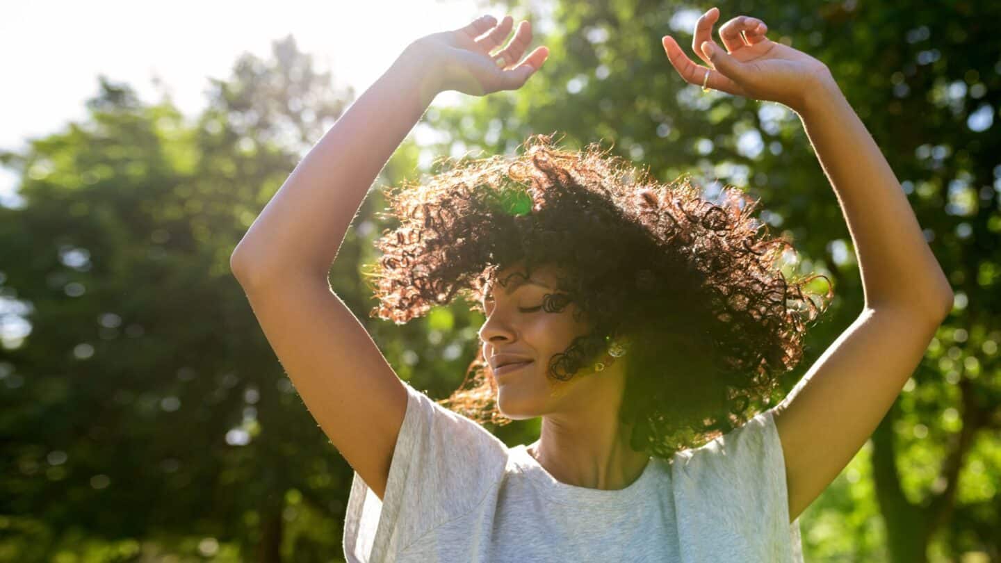 young woman on solo date dancing outside with her arms raised