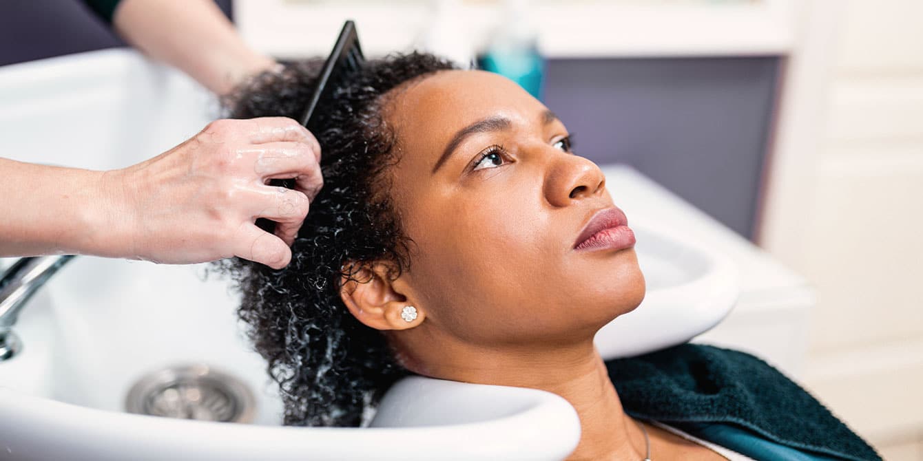 Black woman getting hair washed at the stylist after considering that chemical hair straighteners linked to uterine cancer