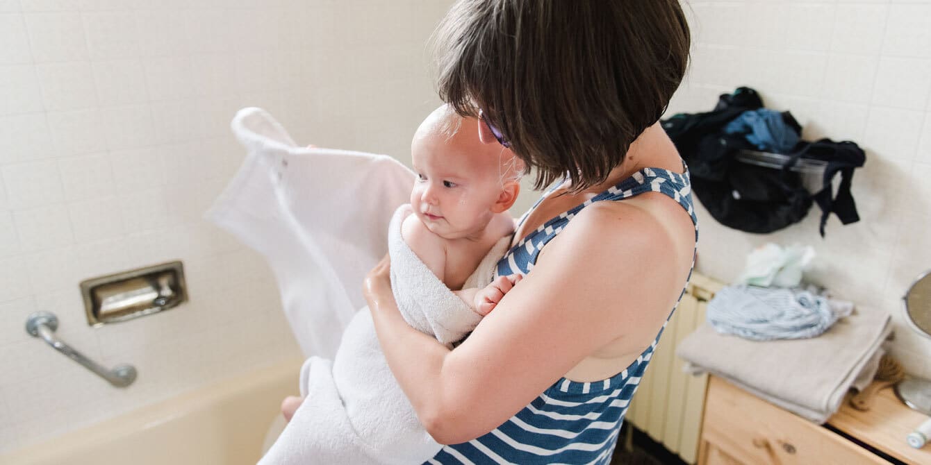 mom holding baby wrapped in a towel - how to give a baby a bath