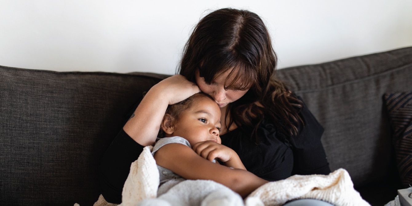 mom holding a little girl on the couch and kissing her head - mental health days