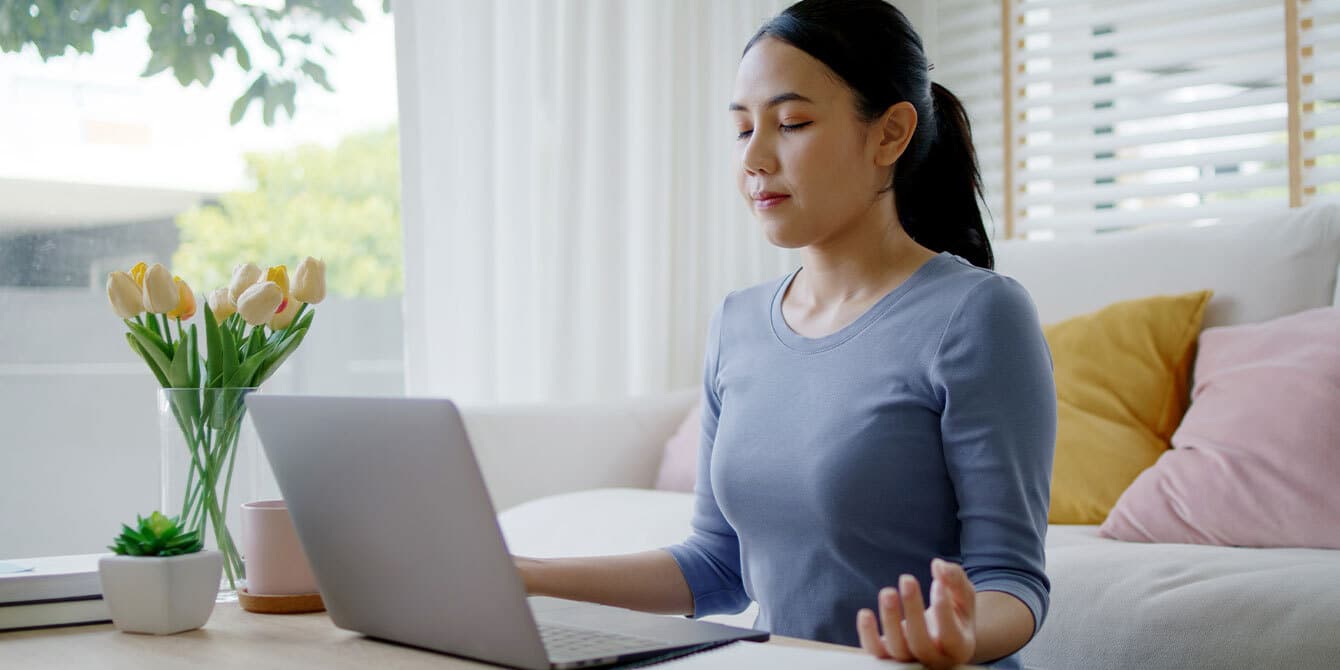 woman coping with anxiety and work stress by meditating in front of a computer