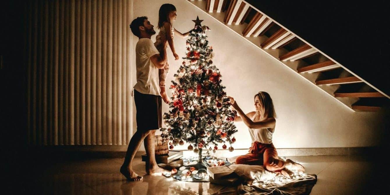 father picking up daughter to put star on tree and mom putting ornaments on- christmas photo ideas