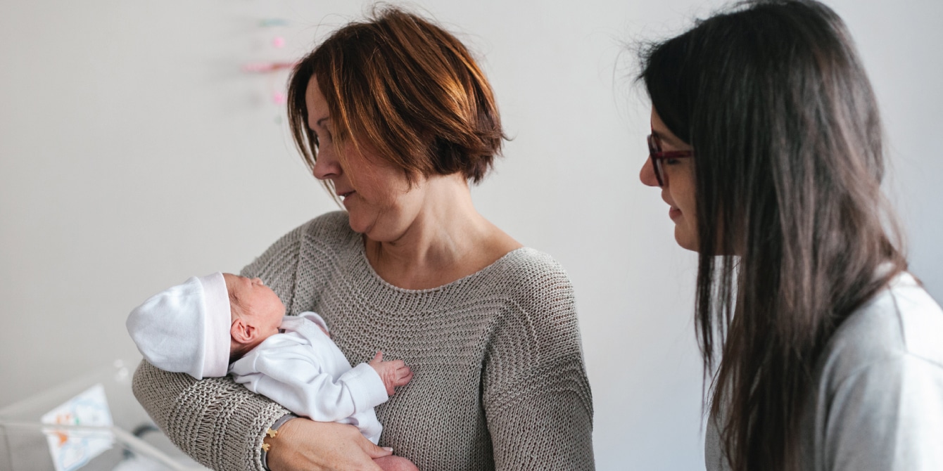 grandmother holding her grandchild while mom looks over - modern parenting