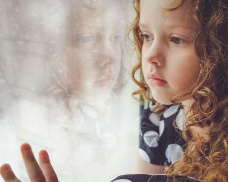 little girl looking out at the snow thru the window