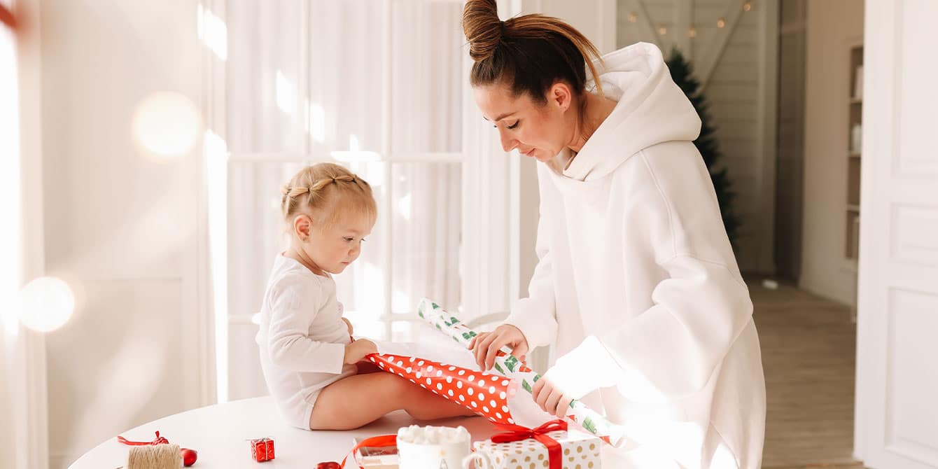 woman showing she is not a pinterest mom wearing oversized hoodie and wrapping gifts with baby