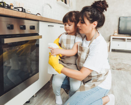 Mom and daughter cleaning stainless steel oven front.