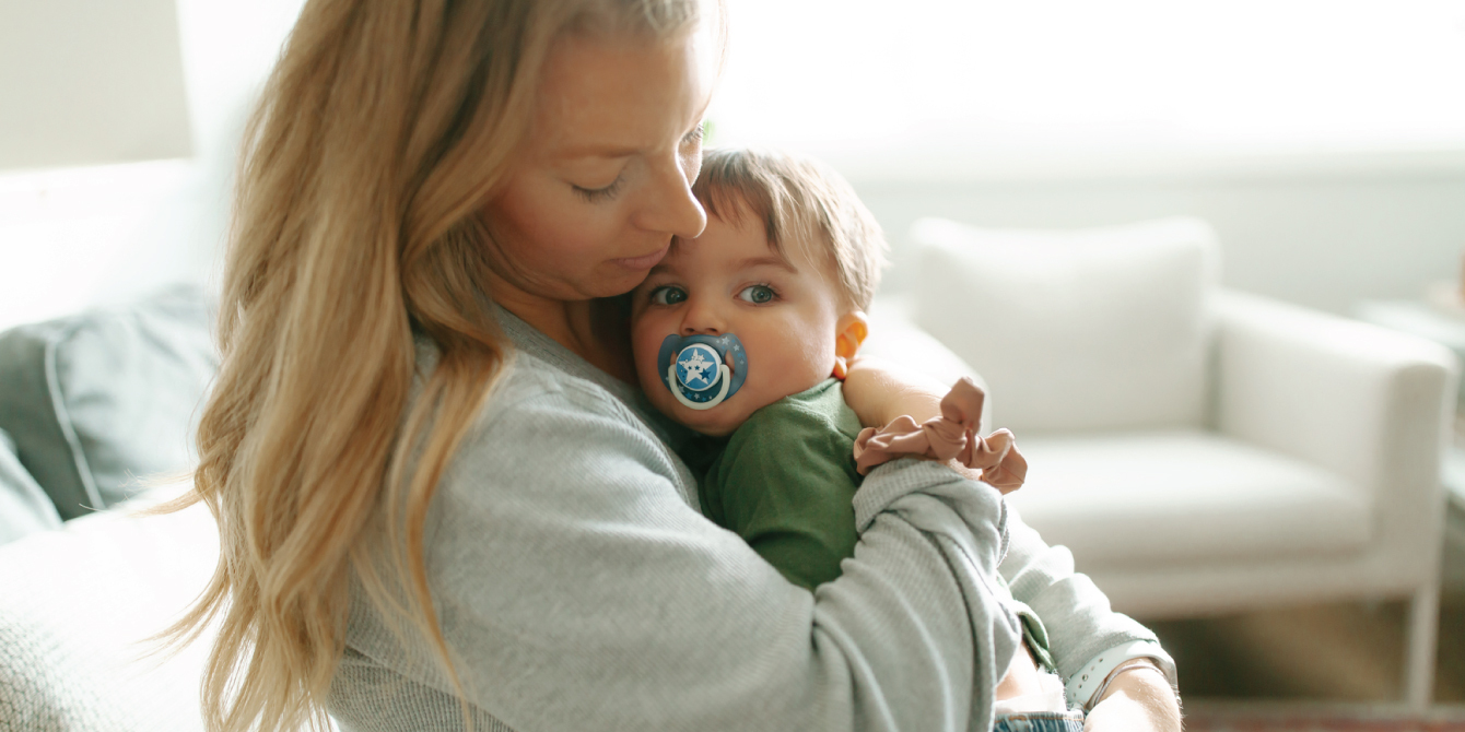 mom hugging a baby with a pacifier against her chest - essay on rsv season