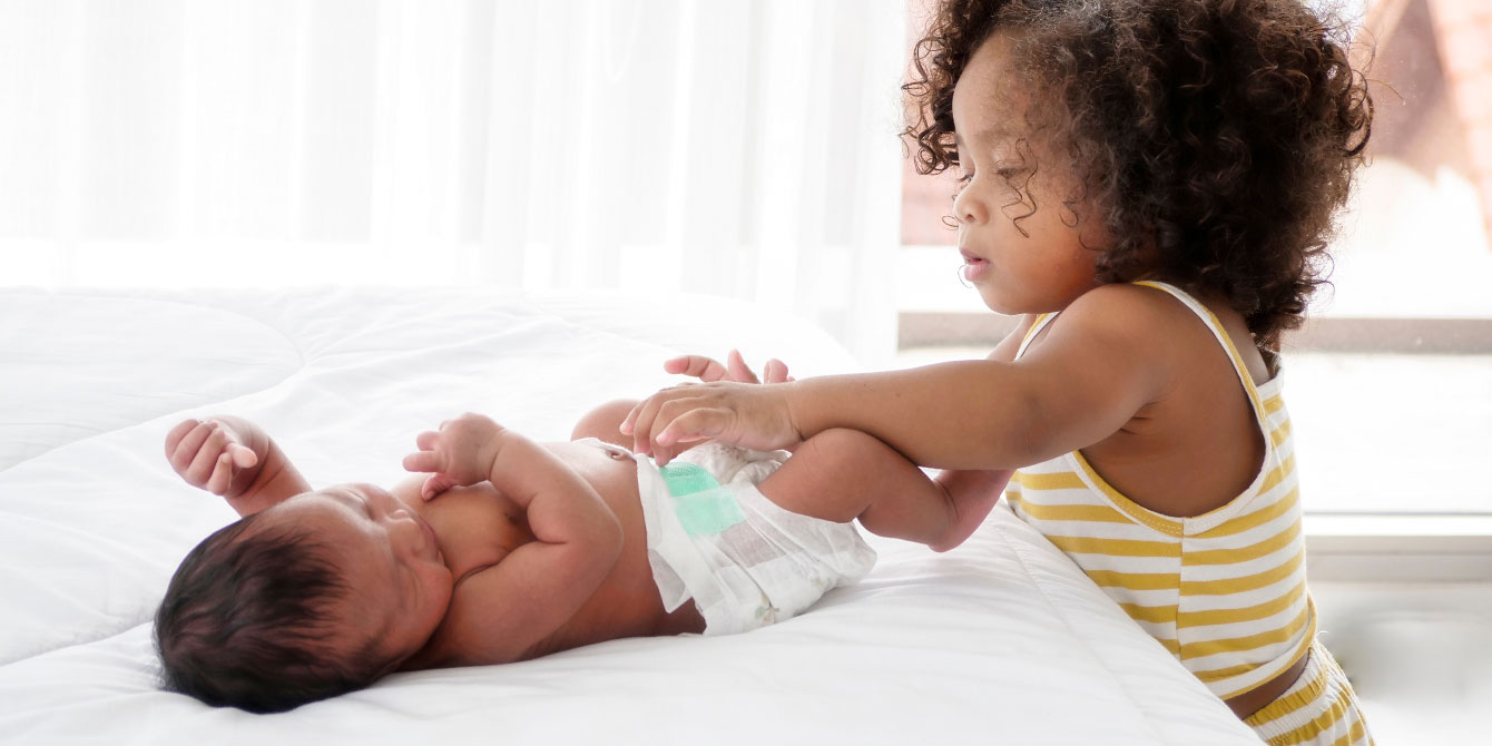 little girl putting diaper on newborn infant baby