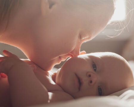 mom kissing her smiling newborn