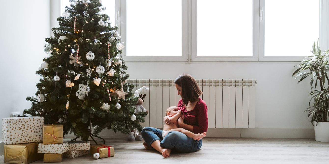 mother breastfeeds her baby by a Christmas tree - keeping newborn routines during holidays consistent