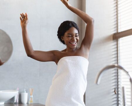 happy woman covered in white towel dancing and laughing in modern bathroom