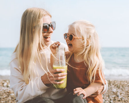 mom and young daughter sharing a smoothie on the beach laughing childhood magic