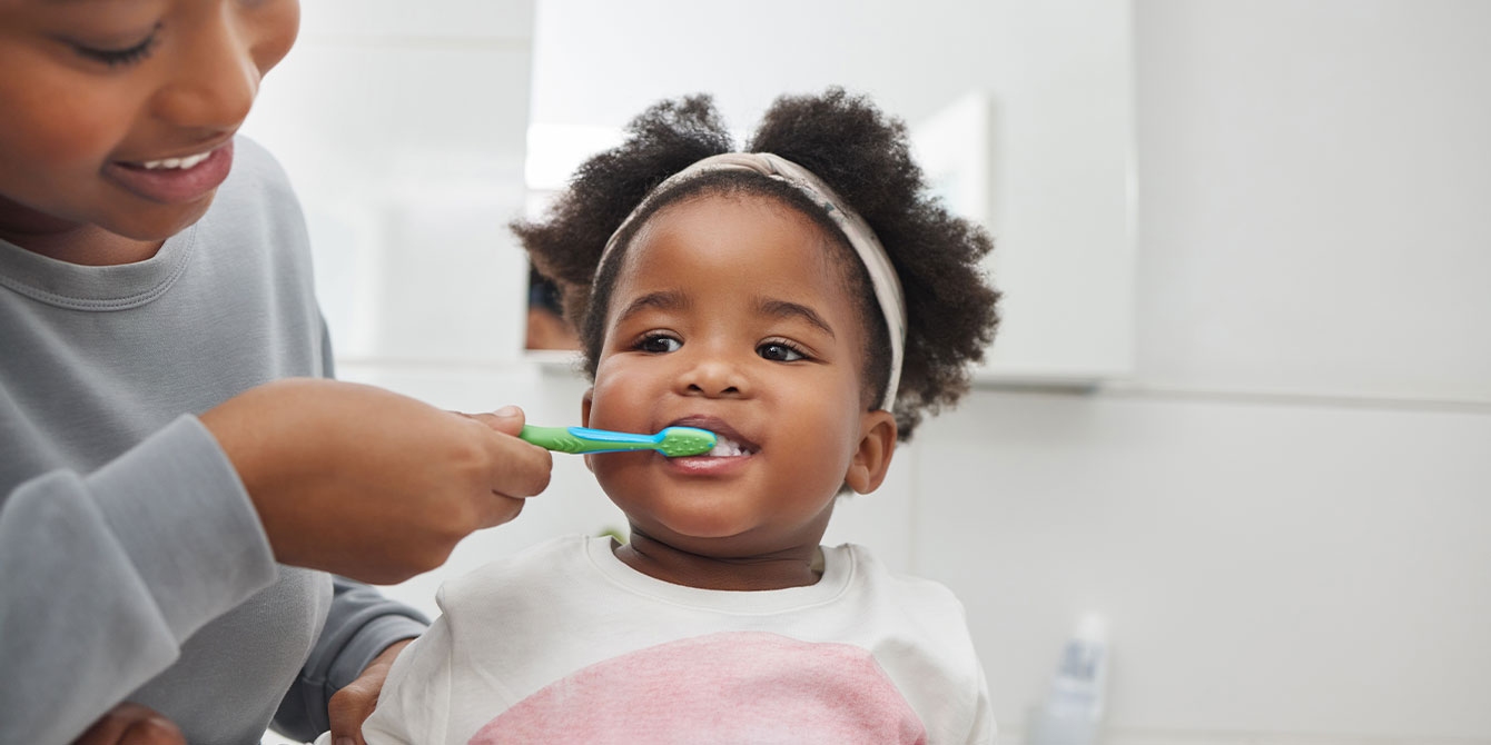 mom helping toddler brush her teeth - habit stacking