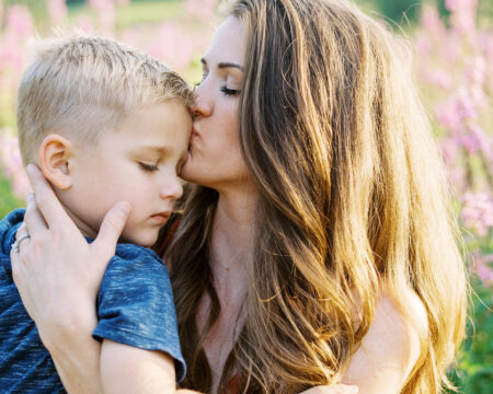 mom kissing son on forehead while sitting in a flower field