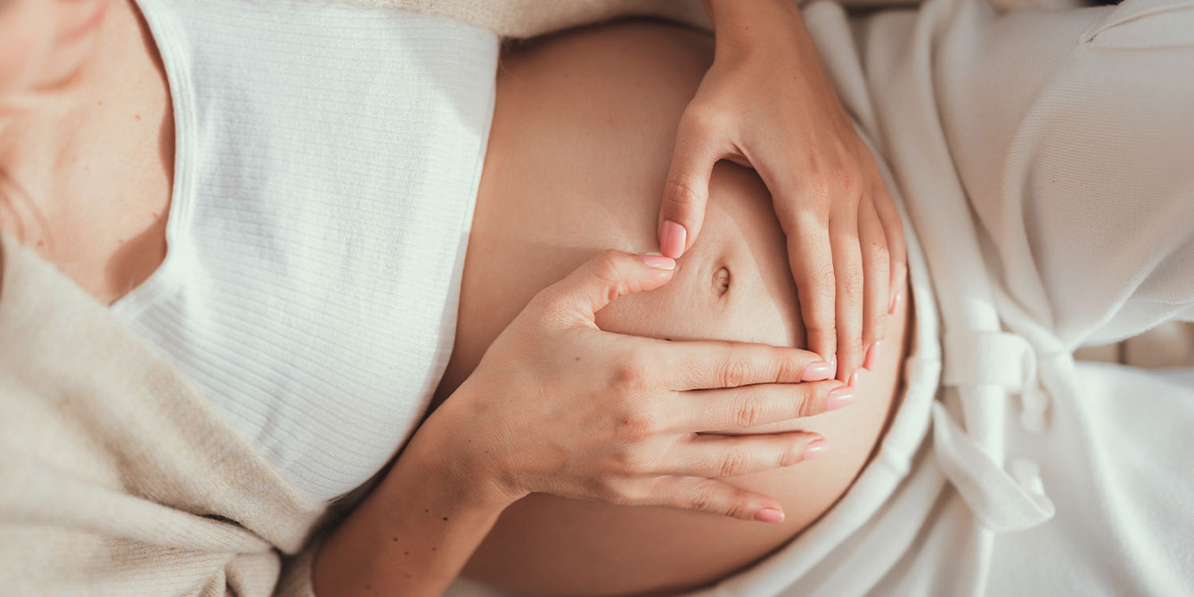 woman holding her pregnant belly making a heart with her hands - can you get pregnant with endometriosis