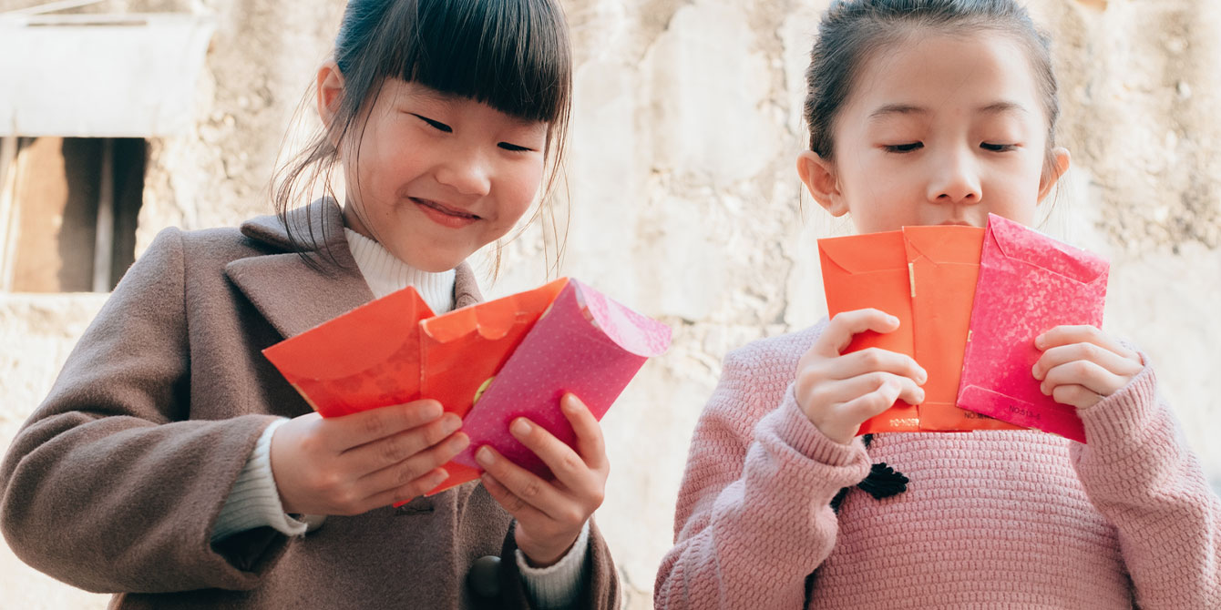 two little girls smiling and holding red chinese new year envelopes- lunar new year crafts