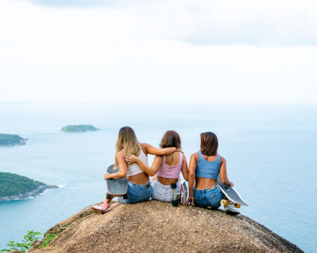 three women sitting on top of a mountain looking at the ocean- mom vacation