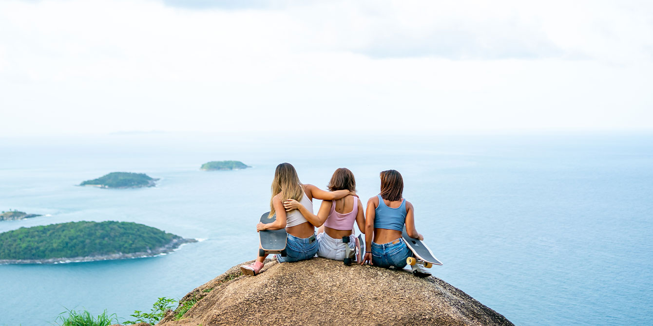 three women sitting on top of a mountain looking at the ocean- mom vacation