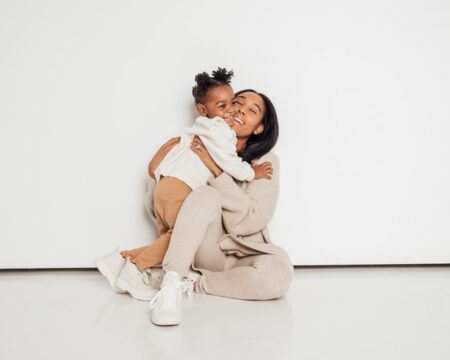 mom and daughter hugging against a white wall Motherly