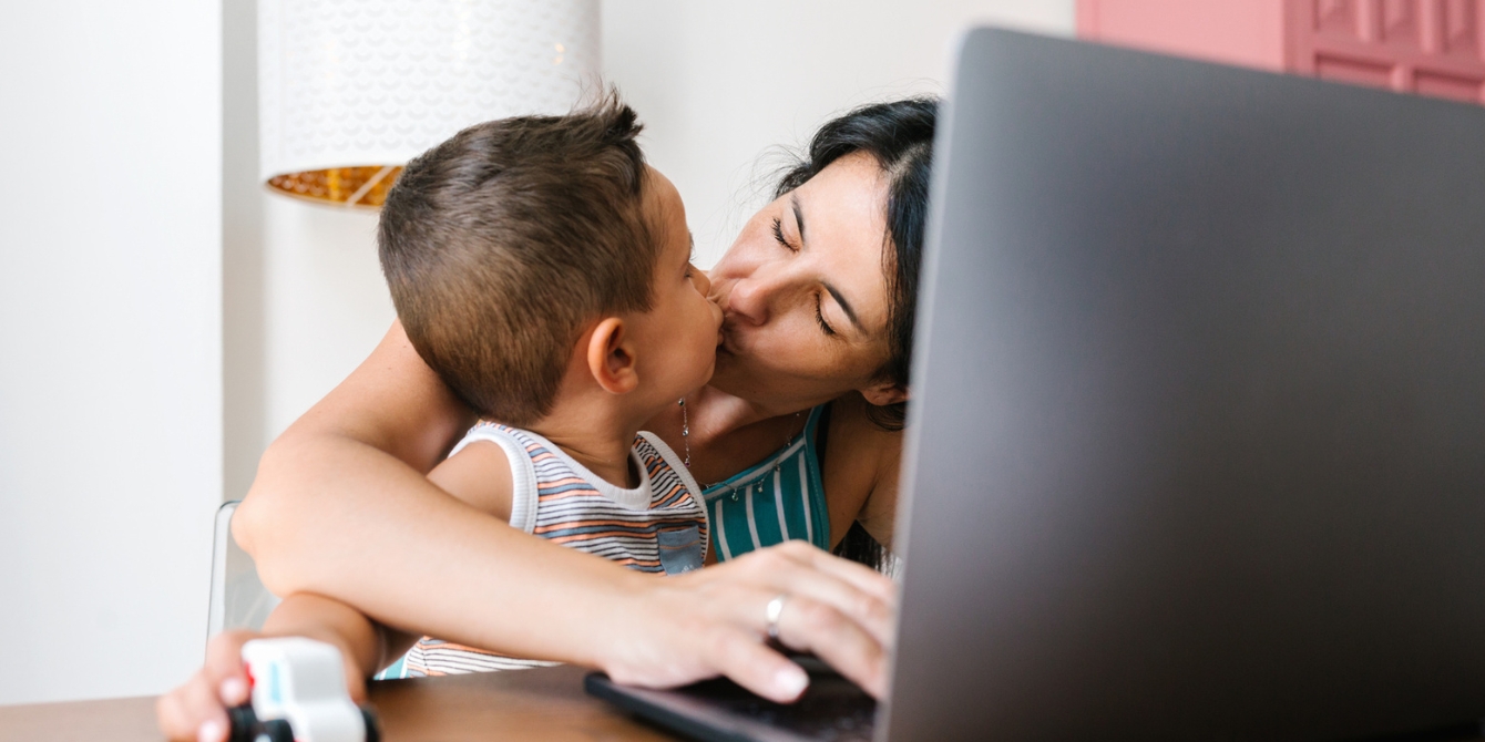 mom kissing child while working on computer- working mom guilt