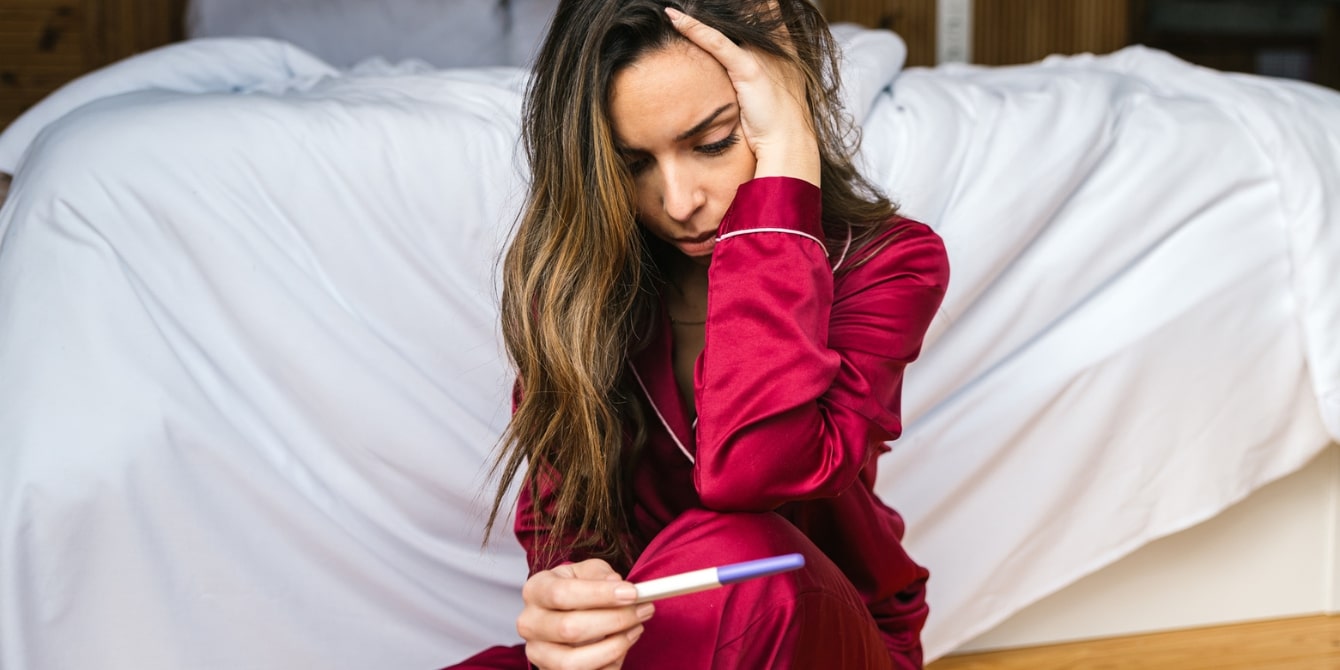 woman looks at pregnancy test at home - stress and fertility
