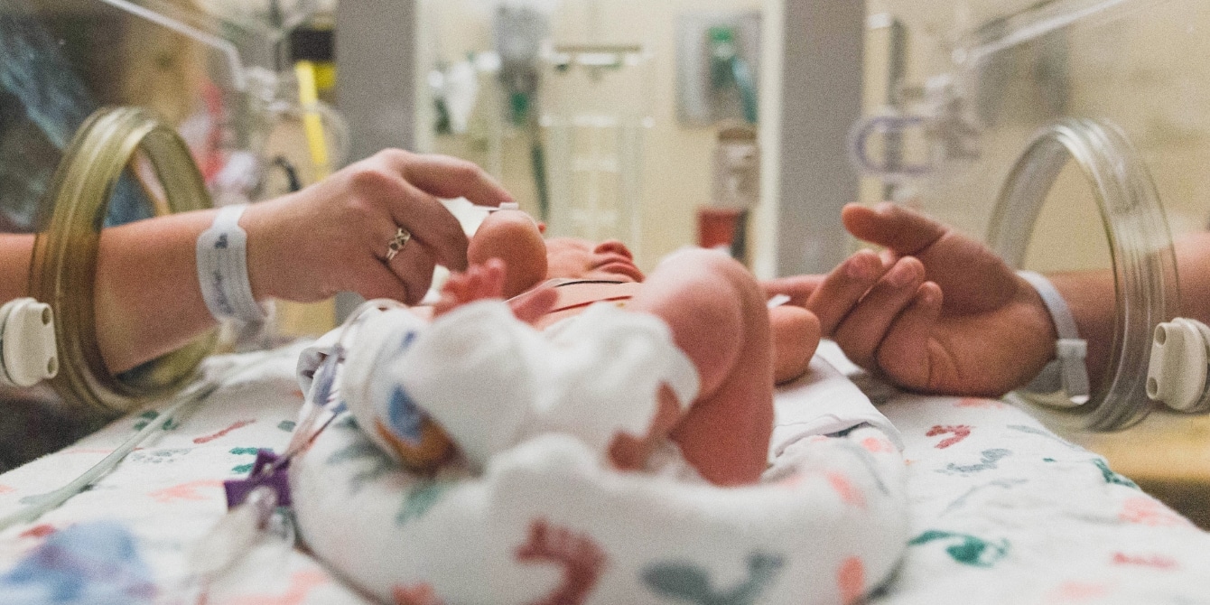 NICU parents touch baby through incubator in NICU