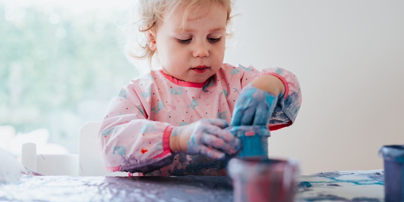 toddler putting hand into a cup of blue fingerpaint