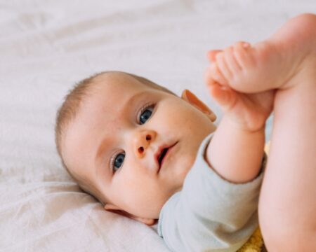 baby girl on bed holding her feet Motherly