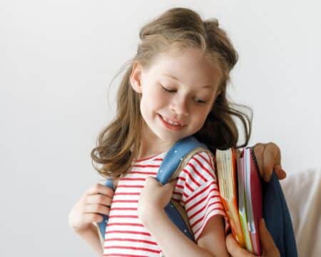 mom putting school supplies in daughters backpack Motherly