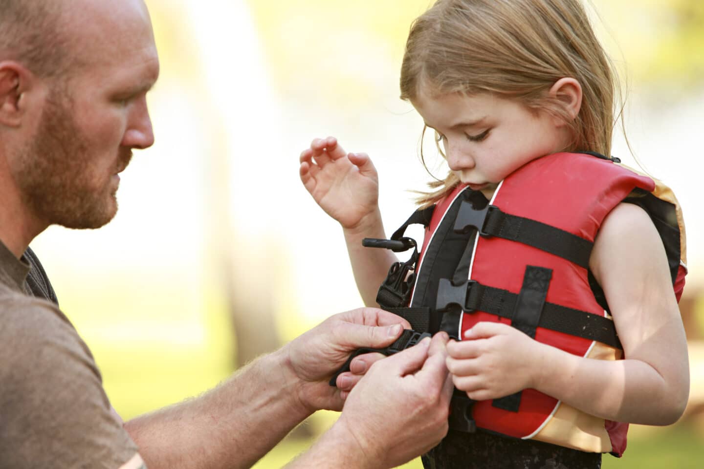 dad buckling daughter into life jacket child safety Motherly