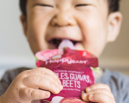 boy in highchair laughing while eating happy baby pouch