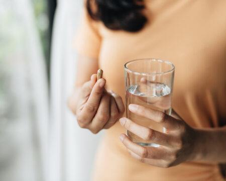 woman taking pill holding glass of water Motherly