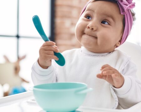 baby sitting in high chair holding spoon Motherly