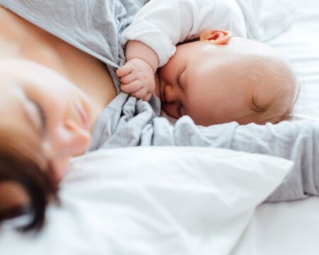 mom lying in bed nursing baby Motherly