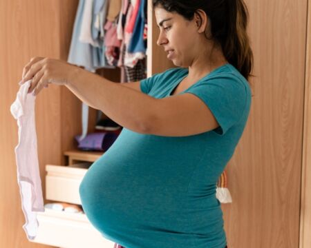 pregnant woman sorting baby clothes Motherly