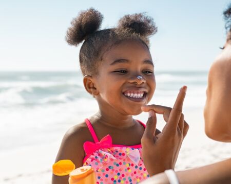 Black mother putting sunscreen on daughter at the beach Motherly