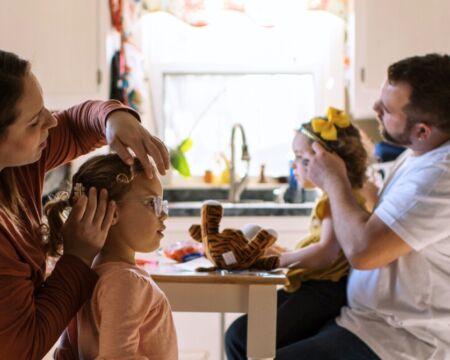 Mother And Father Doing Their Twins Hair Together At Kitchen Table Motherly