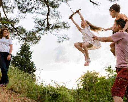 Mother And Father Play With Kids On Tree Swing Motherly